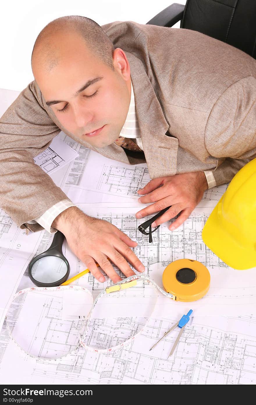 A businessman sleepy with architectural plans at desk