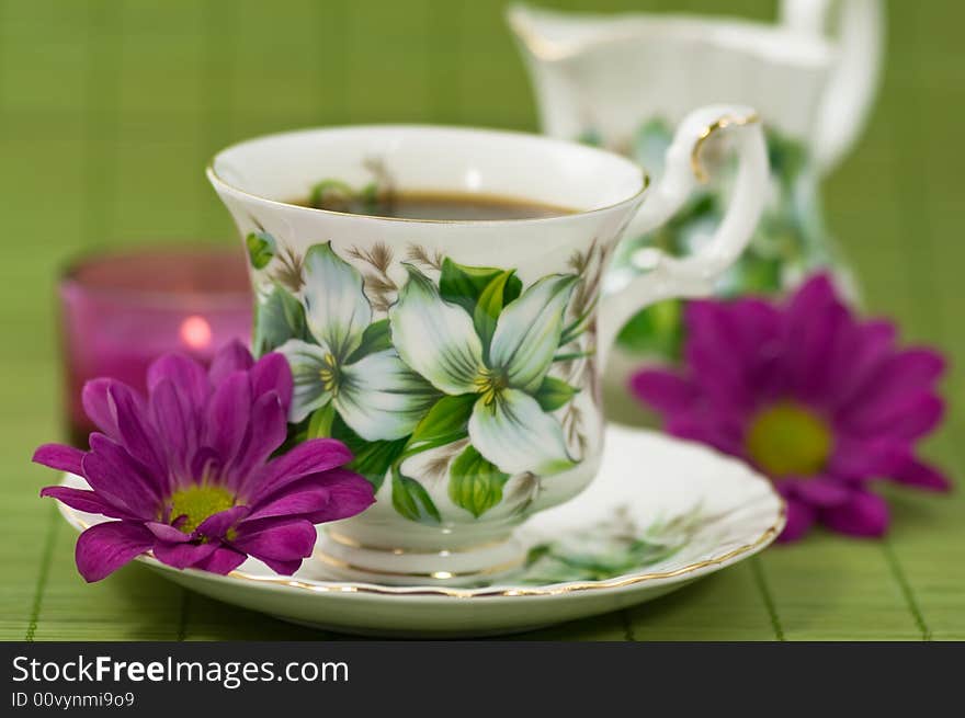 Cup of coffee with creamer, flowers and candle on green background. Cup of coffee with creamer, flowers and candle on green background