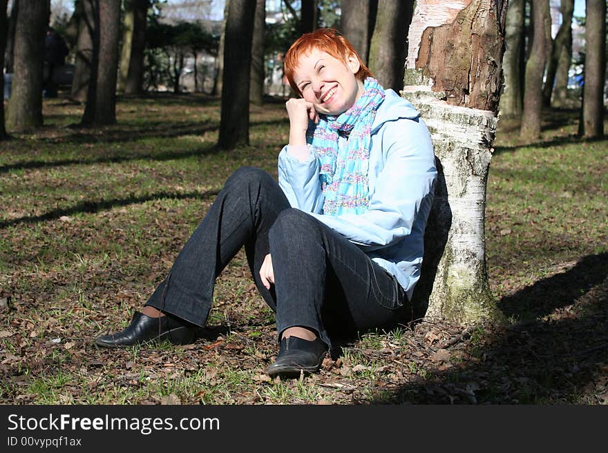 Red haired woman is sitting near tree