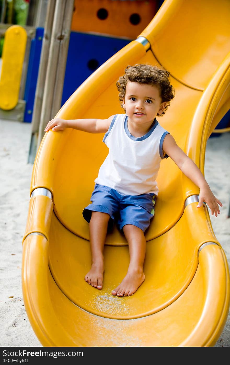 A cute young kid playing on a slide in a park. A cute young kid playing on a slide in a park