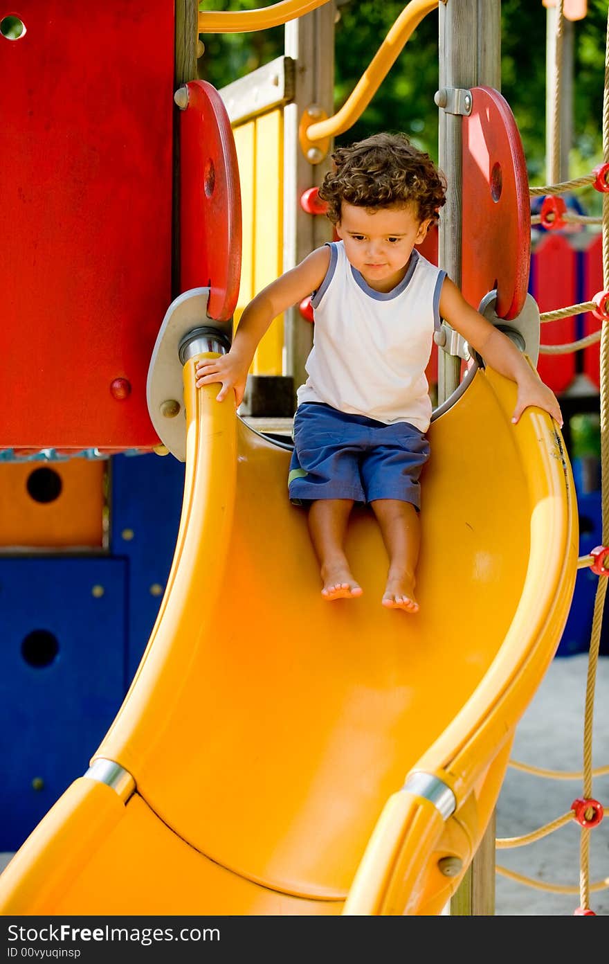A cute young kid playing on a slide in a park. A cute young kid playing on a slide in a park