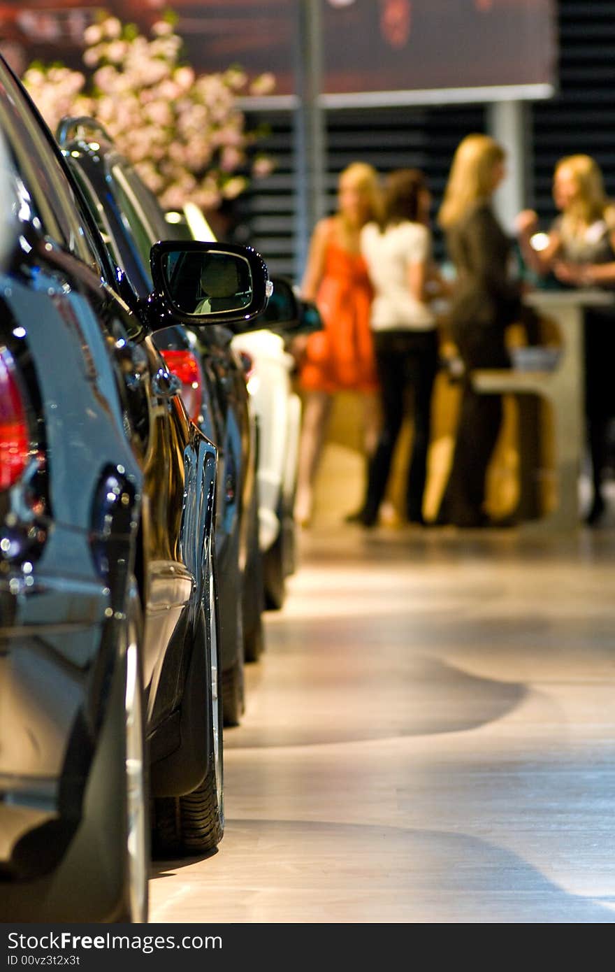 Row of new cars at this year's biggest motorshow in the Baltics. Visitors consulting sales department in the background. Row of new cars at this year's biggest motorshow in the Baltics. Visitors consulting sales department in the background.