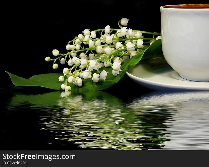 Flowers of a llies of the valley and white cup of black coffee on a black background. Flowers of a llies of the valley and white cup of black coffee on a black background