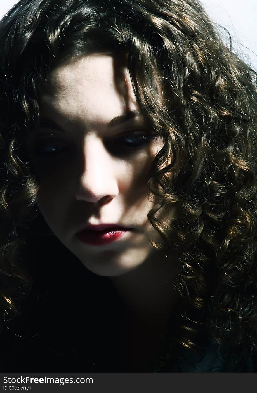 A low-key portrait about a pretty lady with white skin and long brown wavy hair who is looking down and she is lost in thought. A low-key portrait about a pretty lady with white skin and long brown wavy hair who is looking down and she is lost in thought