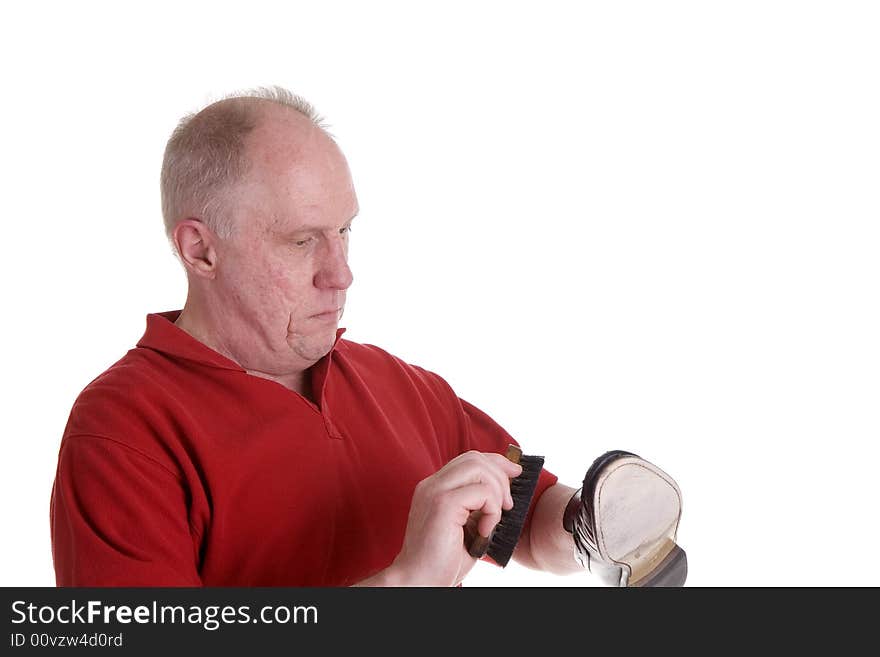 An older guy in a red shirt with a shoe and shoeshine brush on a white background. An older guy in a red shirt with a shoe and shoeshine brush on a white background