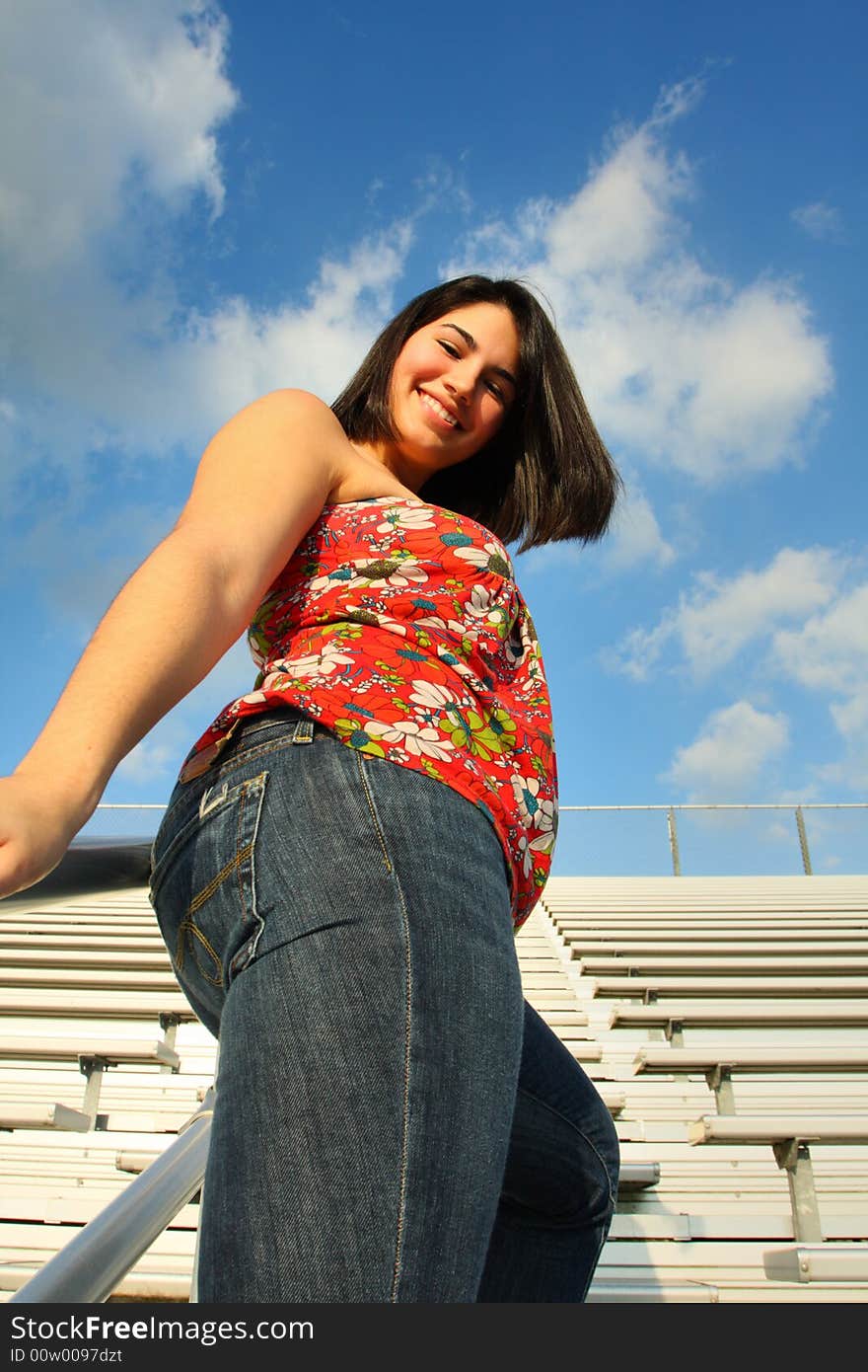 Woman standing by sporting bleachers and a blue sky background. Woman standing by sporting bleachers and a blue sky background.