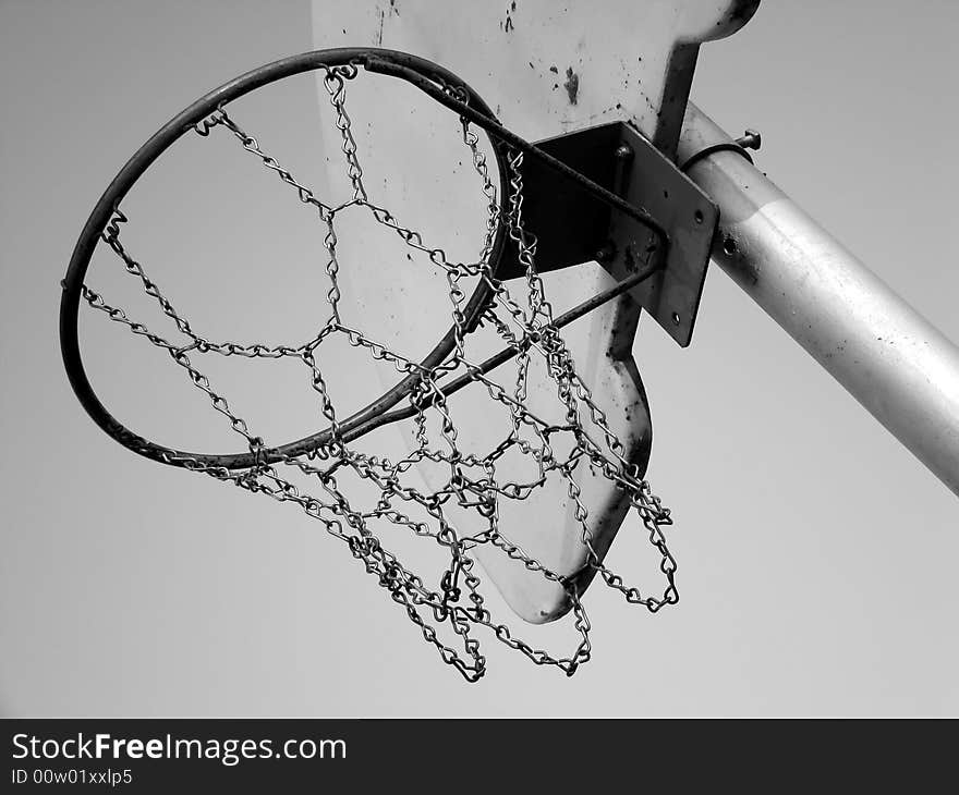 Black and white image at a slant of basketball hoop and backboard on playground