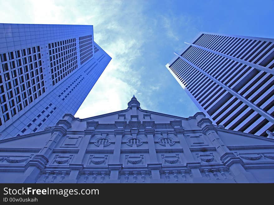 Futuristic skyscrapers tower over a small unique building. Futuristic skyscrapers tower over a small unique building.