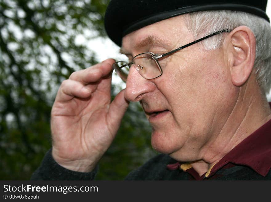 A senior with glasses and flatcap with his hand up to his face. A senior with glasses and flatcap with his hand up to his face