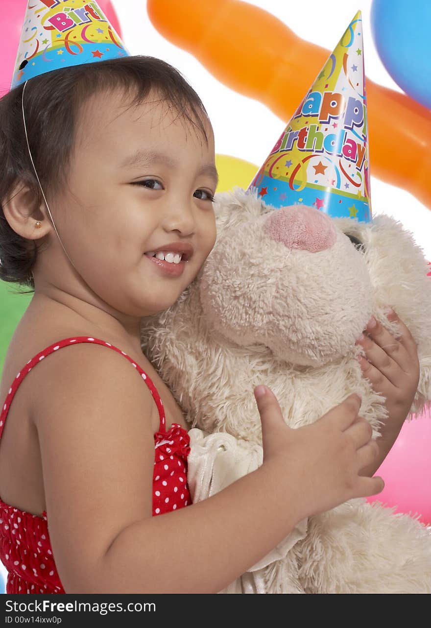 Young girl holding teddy bear with party hat