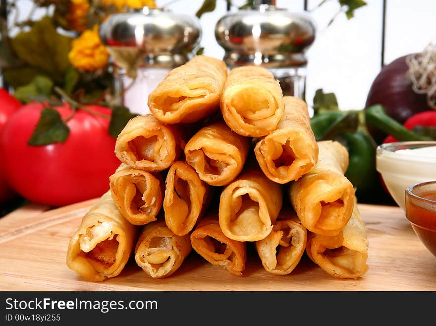 Stack of chicken taquitos with hot sauce and sour cream in kitchen or restaurant