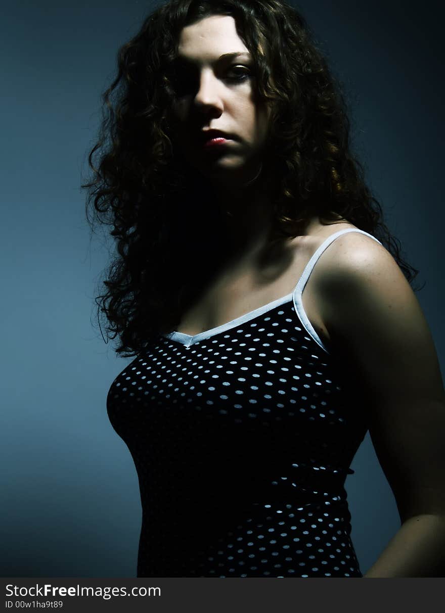 A dark low-key portrait about a pretty lady with white skin and long brown wavy hair whose look is strongly attractive and she wears a nice black dress with white dots. A dark low-key portrait about a pretty lady with white skin and long brown wavy hair whose look is strongly attractive and she wears a nice black dress with white dots