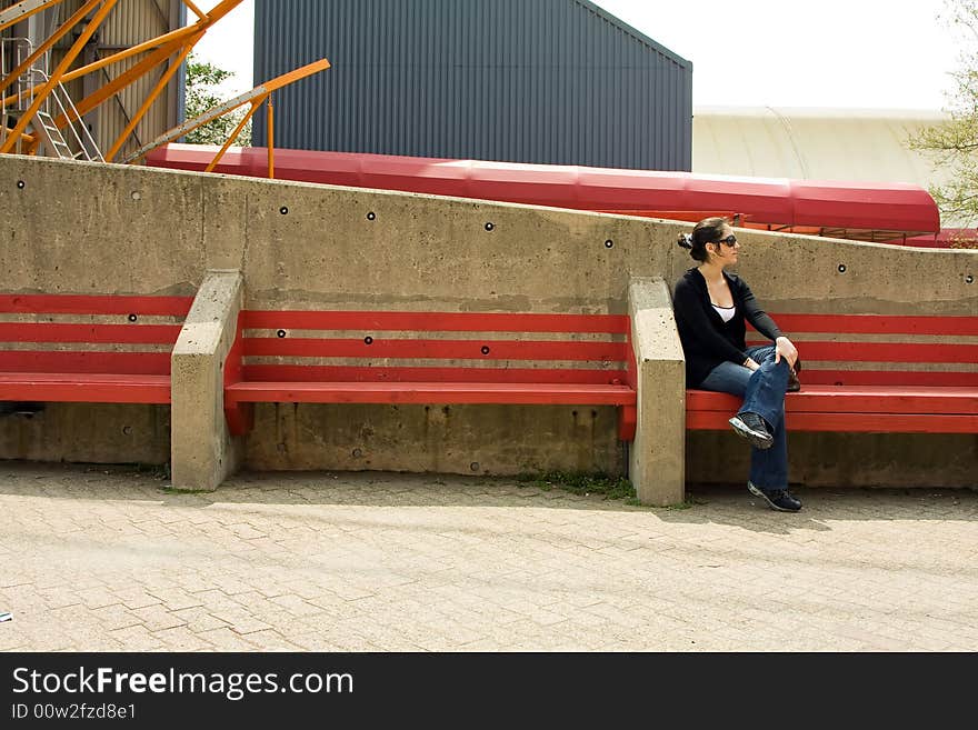 Beautiful young woman sitting/waiting on a red bench on a bright day, wearing sunglasses. Beautiful young woman sitting/waiting on a red bench on a bright day, wearing sunglasses