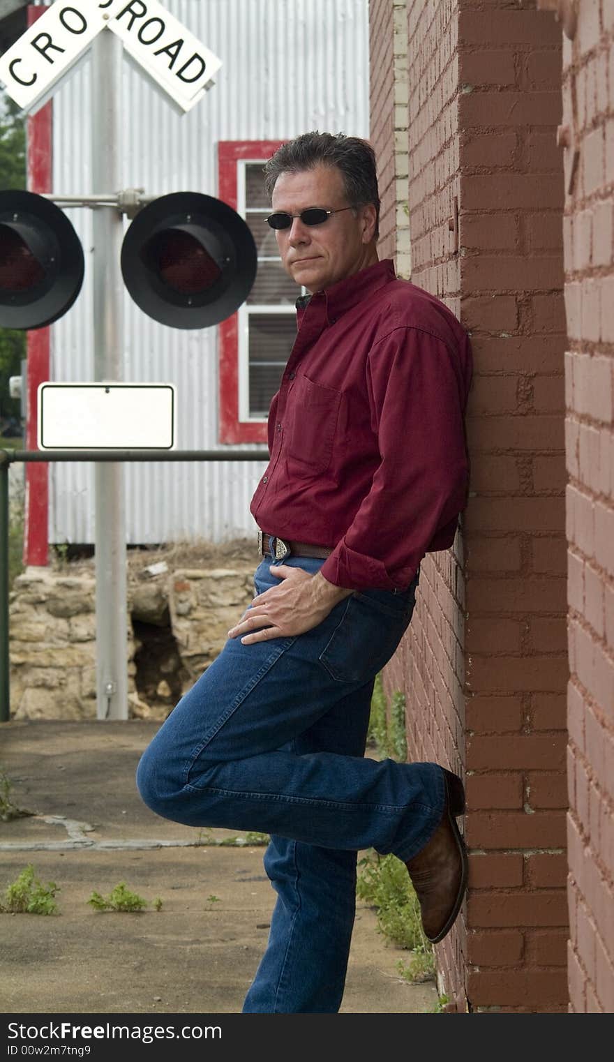 A man leaning up against a red brick wall with a railroad crossing warning signal in the background. A man leaning up against a red brick wall with a railroad crossing warning signal in the background.