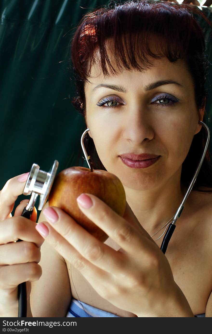 Young woman examining apple with stethoscope. Young woman examining apple with stethoscope