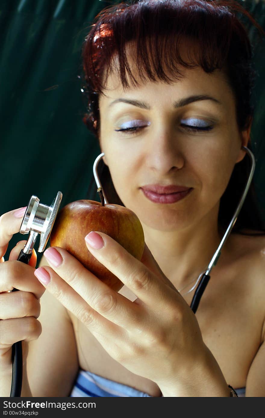 Young woman examining an apple by using a stethoscope. Young woman examining an apple by using a stethoscope