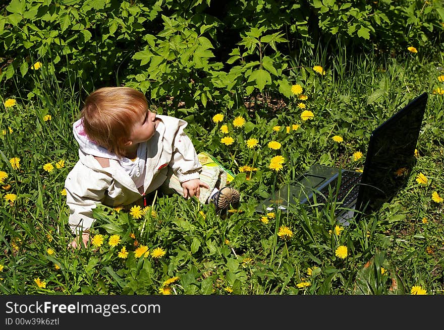 The little girl sits on a grass near to laptop. The little girl sits on a grass near to laptop