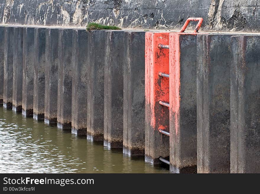 The ladder between the vertical rusted steel ribs of a Lake Michigan pier, it's fluorescent red paint chipped and peeling. The ladder between the vertical rusted steel ribs of a Lake Michigan pier, it's fluorescent red paint chipped and peeling