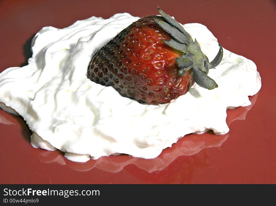 A strawberry on a bed of whipped cream on a red plate. A strawberry on a bed of whipped cream on a red plate.