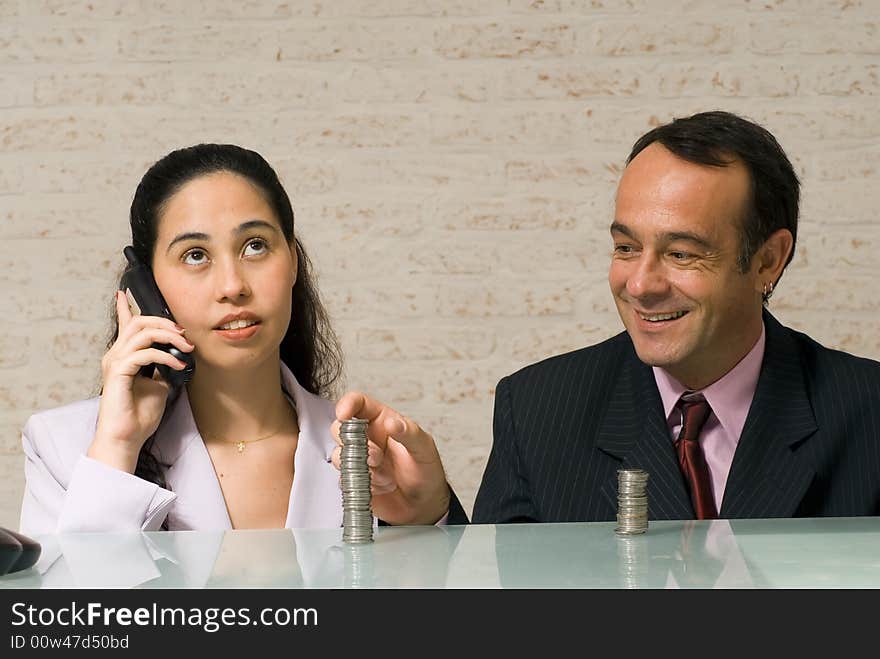 Businessman reaching over and stealing money playfully from his female colleague while she talks on the phone. Businessman reaching over and stealing money playfully from his female colleague while she talks on the phone