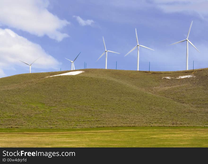 Five modern windmills sit on top of a green hill in spring. Five modern windmills sit on top of a green hill in spring.