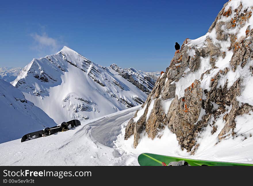 Winter mountain scenery with two snowboards and black bird on the rock. Winter mountain scenery with two snowboards and black bird on the rock