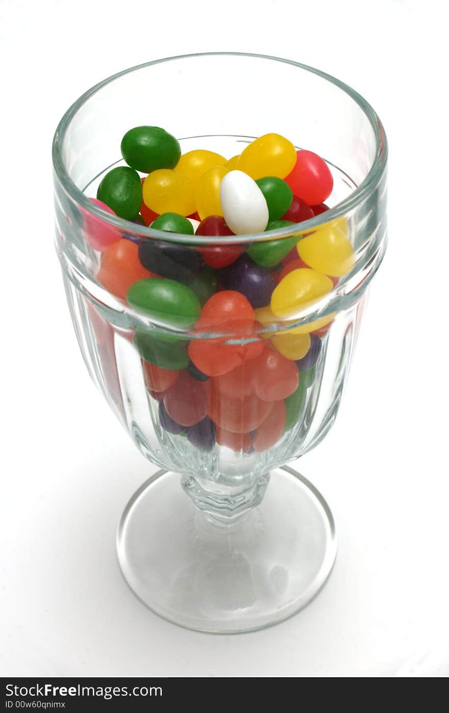 A glass sundae cup mostly filled with colorful jelly beans. The view is from slightly above, vertically oriented over white. A glass sundae cup mostly filled with colorful jelly beans. The view is from slightly above, vertically oriented over white.