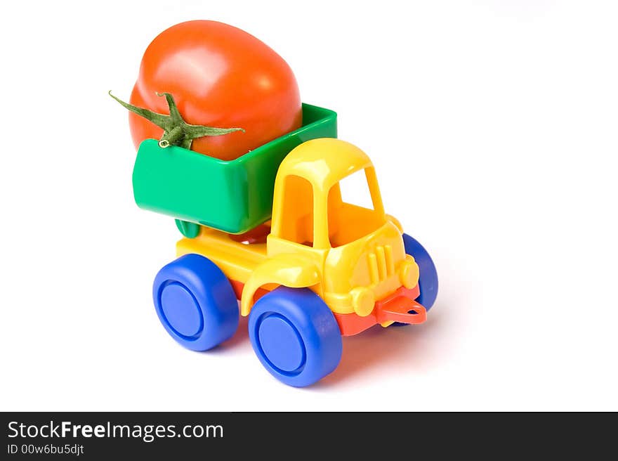 A photo of a little toy lorry carrying a tomato. A photo of a little toy lorry carrying a tomato