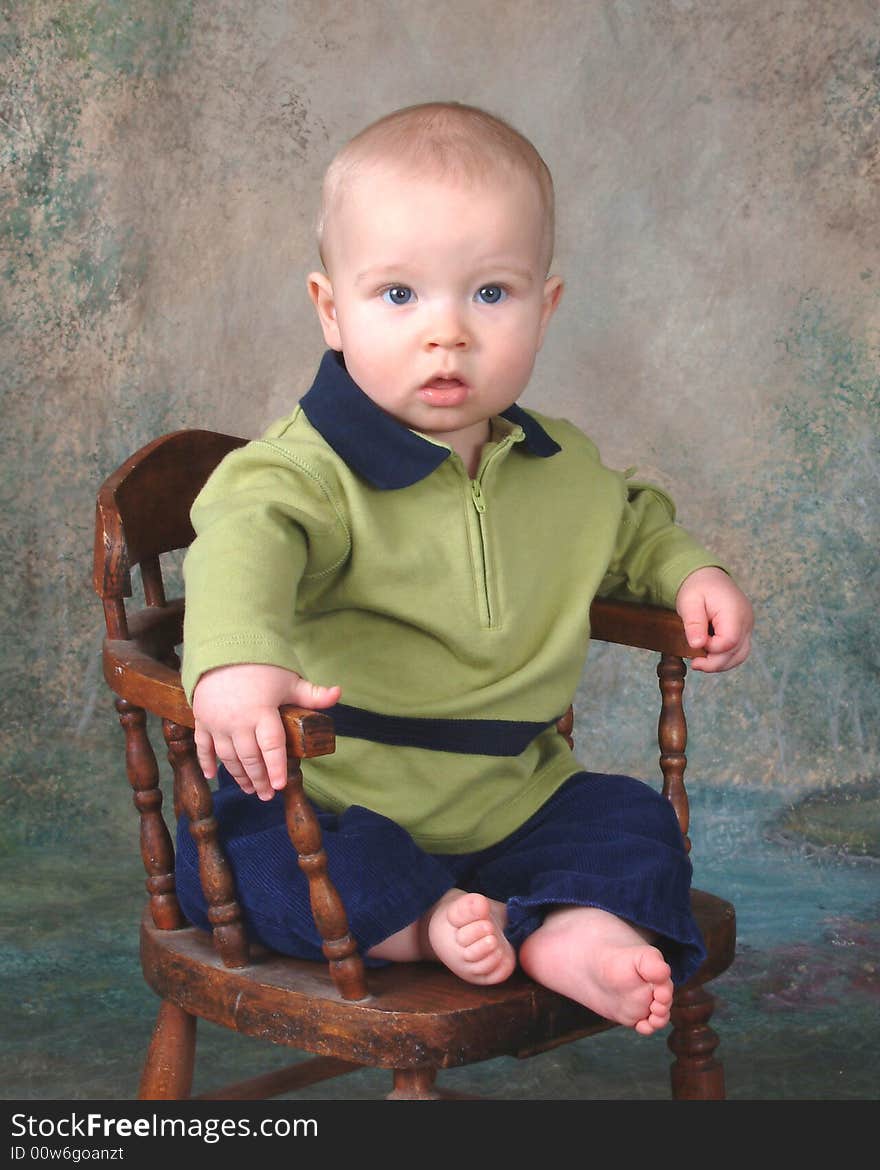 Baby boy sitting in front of muslin background on old wooden chair. Baby boy sitting in front of muslin background on old wooden chair