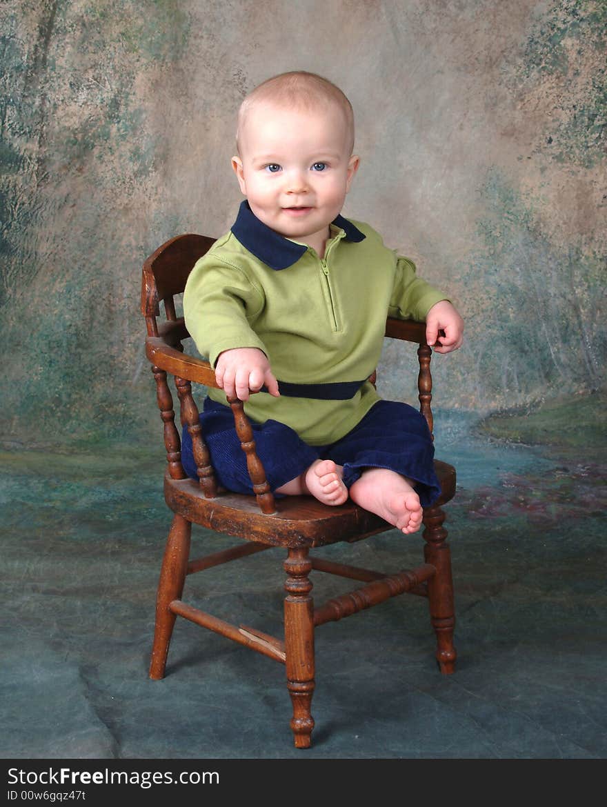 Baby boy sitting in front of muslin background on old wooden chair. Baby boy sitting in front of muslin background on old wooden chair