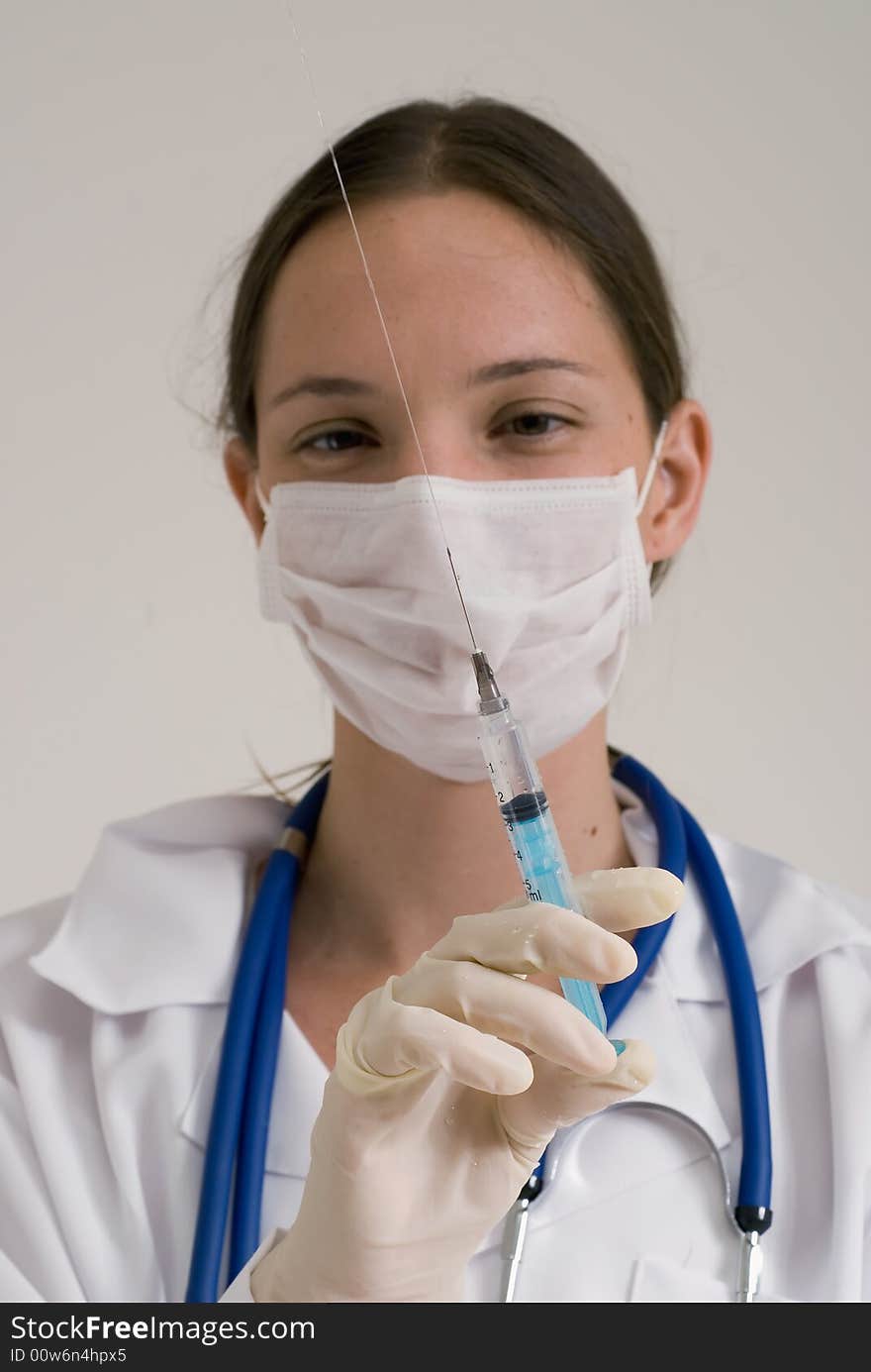 Young female doctor wearing a surgical mask and holding a syringe in the air. Young female doctor wearing a surgical mask and holding a syringe in the air