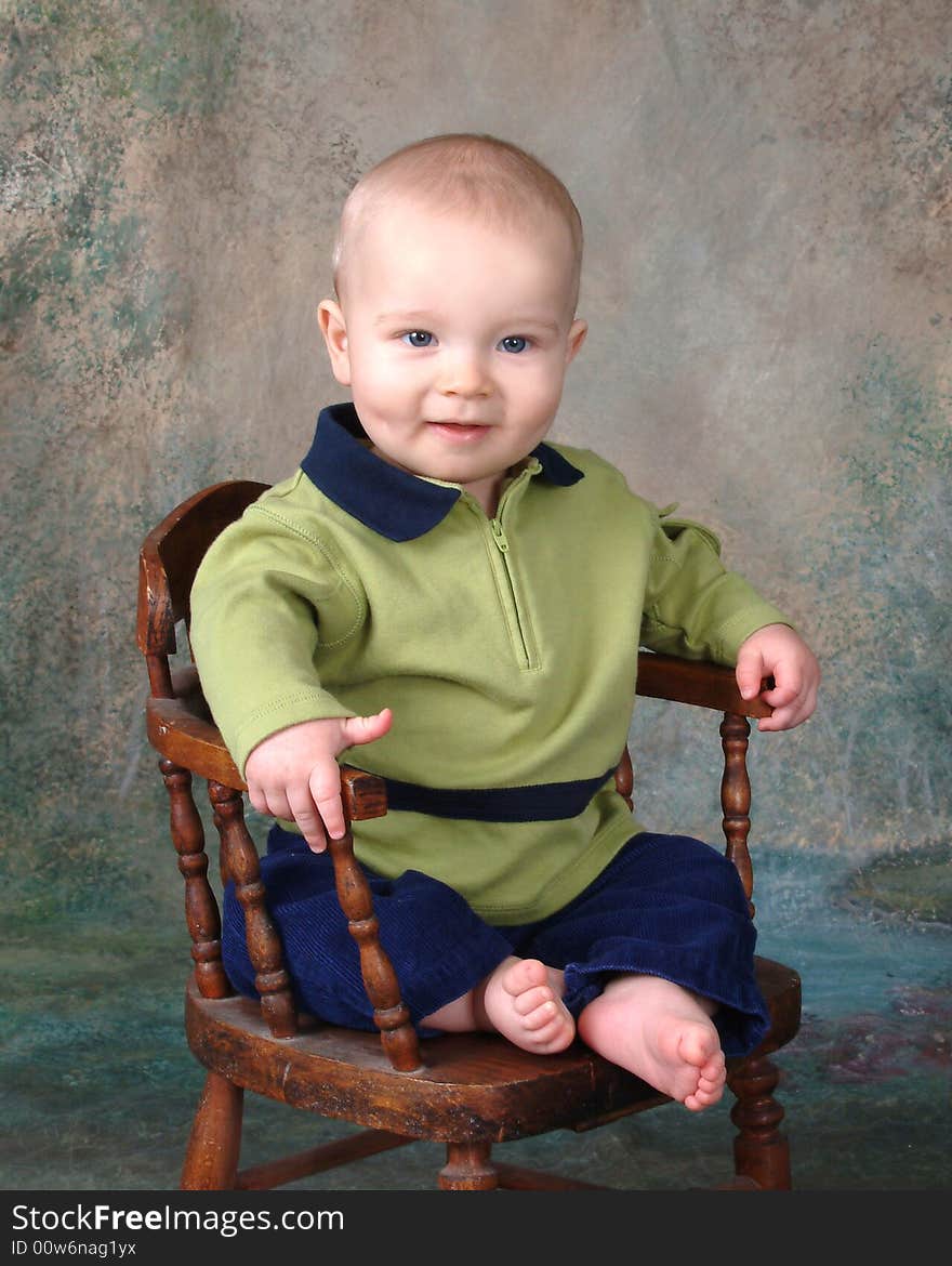 Baby boy sitting in front of muslin background on old wooden chair. Baby boy sitting in front of muslin background on old wooden chair