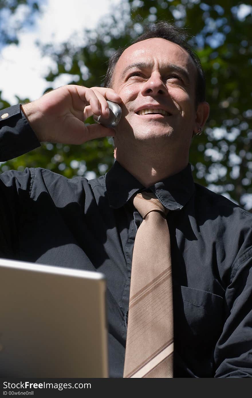 Latin american business man on the phone with his laptop computer open in front of him. Latin american business man on the phone with his laptop computer open in front of him