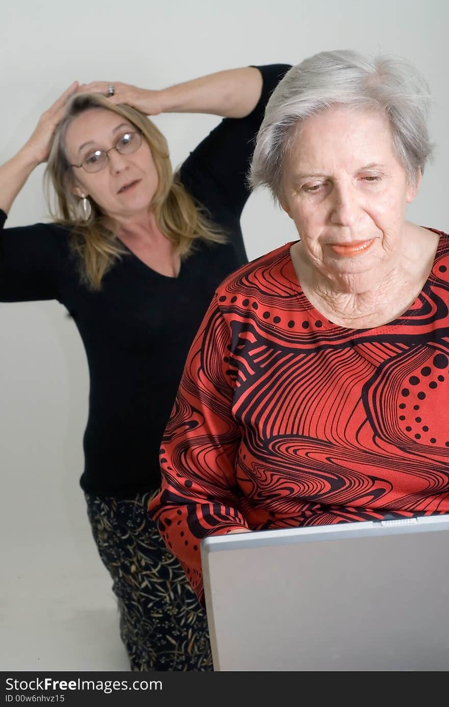 Woman looking over her elderly mother's shoulder while the older lady is working on a laptop. Woman looking over her elderly mother's shoulder while the older lady is working on a laptop