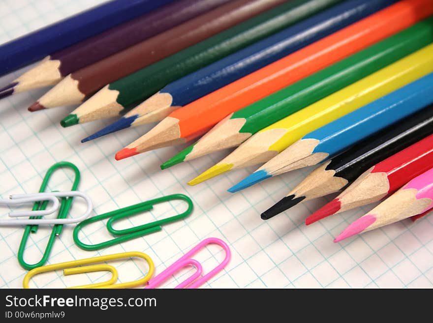 Color pencils and clips on a checkered paper.