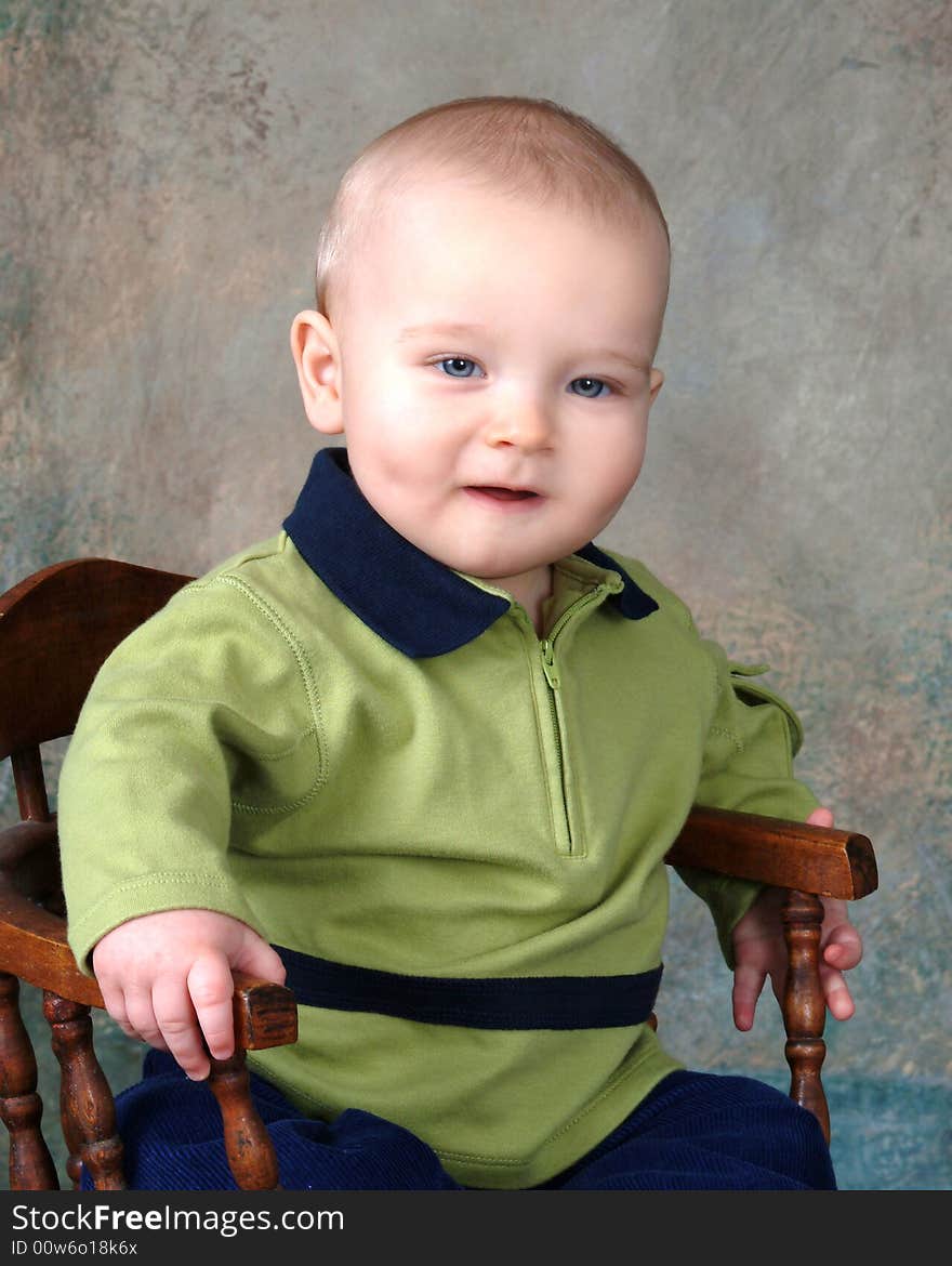Baby boy sitting in front of muslin background on old wooden chair. Baby boy sitting in front of muslin background on old wooden chair