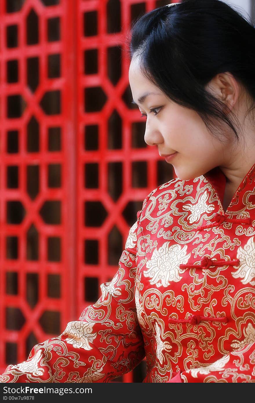 A Chinese girl in traditional dress ponders in front of the ancient window.