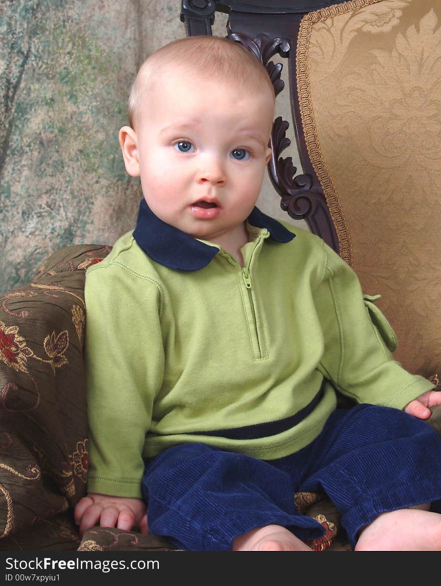 Baby boy sitting in front of muslin background on old antique chair. Baby boy sitting in front of muslin background on old antique chair