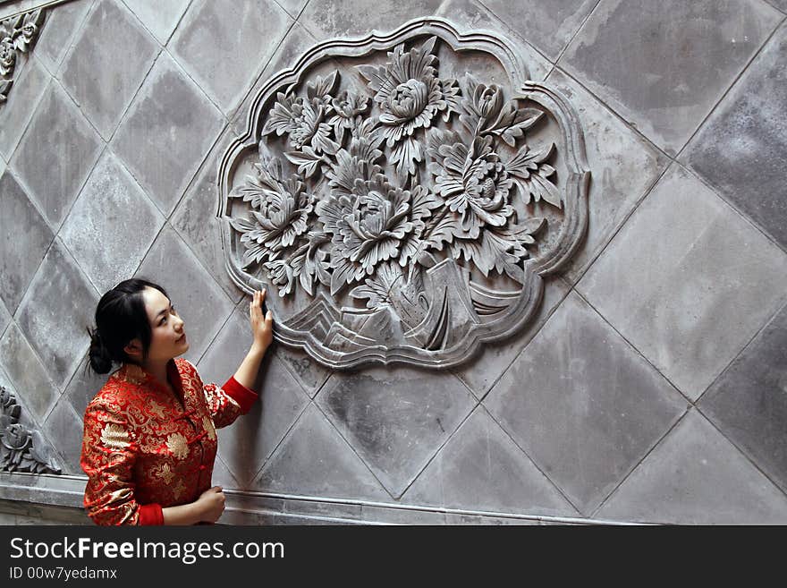 A Chinese girl in traditional dress stands in front of the ornamental wall of the ancient courtyard of China.

The ornamental wall is the important ornamental wall in the ancient courtyard gate of China, mainly play a protective screen role, beautify the entry to the gate. Its pattern is a kind of lucky symbol.