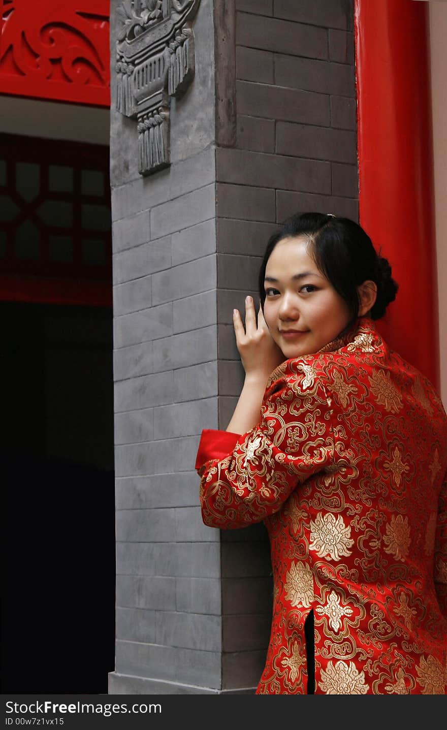 A Chinese girl in traditional dress stands at the front door of the ancient courtyard of China. Perhaps she is longing for the future.