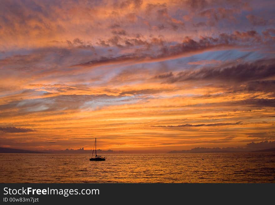 A small sailboat drifts into an all-encompassing tropical sunset. A small sailboat drifts into an all-encompassing tropical sunset