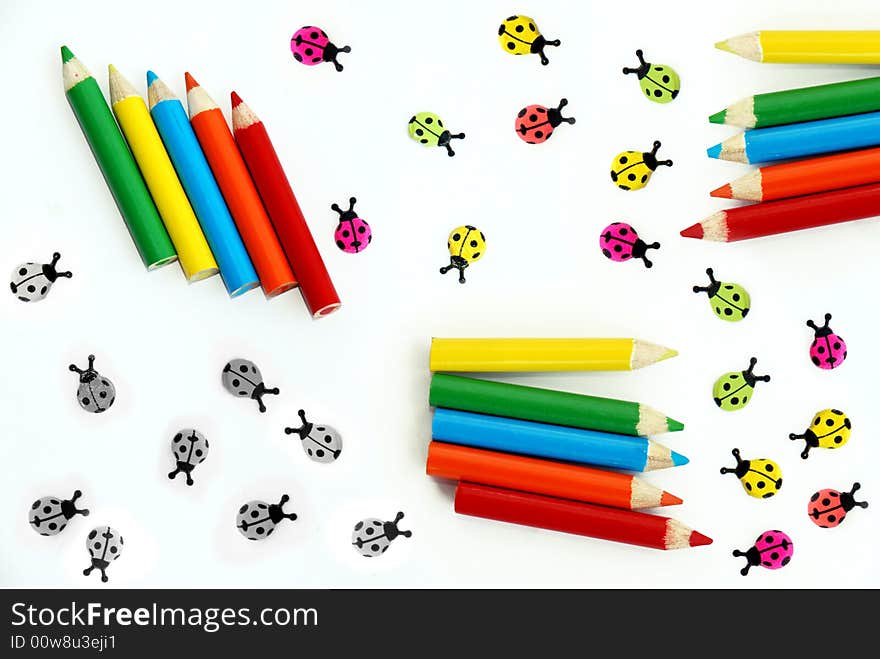 Various small colored pencils and ladybirds over white background isolated