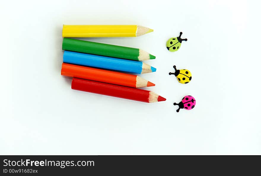 Various small colored pencils and ladybirds over white background isolated