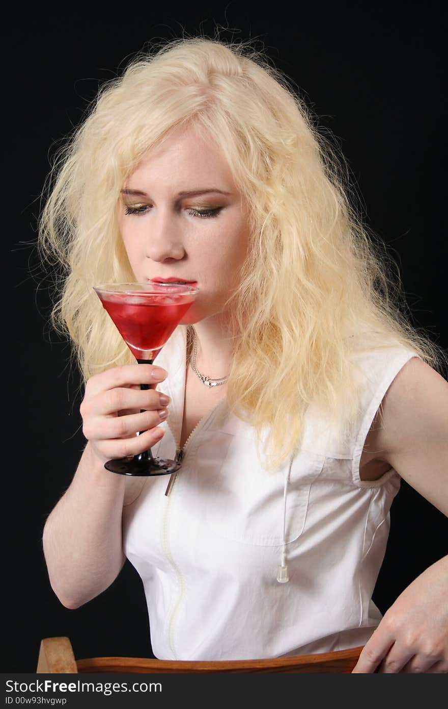 Young blond woman holds martini against the black background. Young blond woman holds martini against the black background