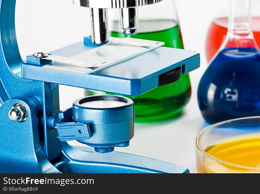 Various colorful flasks and blue microscope over white background