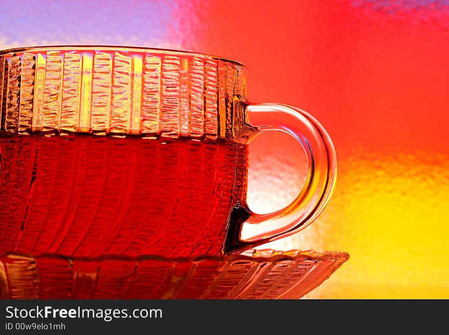 Close-up of glass teacup and saucer against multi colored abstract background