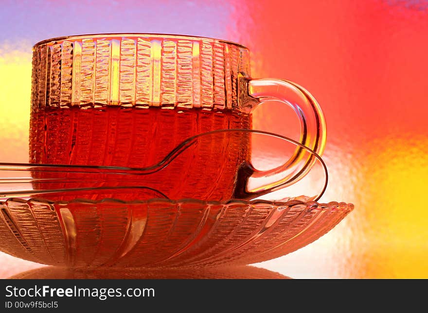 Close-up of glass teacup, saucer and spoon against multi colored abstract background