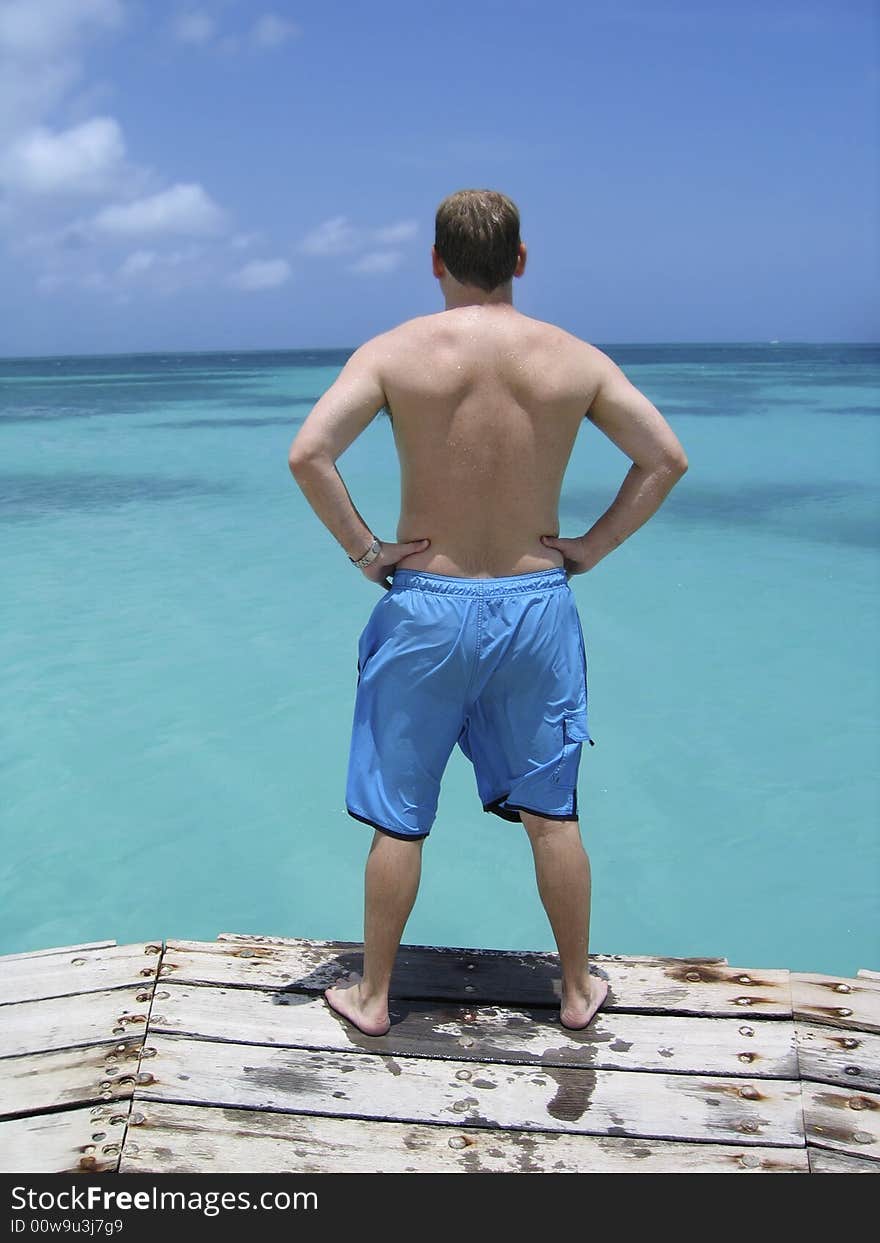 A man ponders jumping into the crystal blue waters of the Caribbean ocean from a wood deck. A man ponders jumping into the crystal blue waters of the Caribbean ocean from a wood deck.