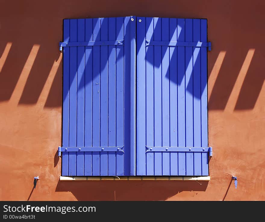 Bright blue shutters against terracotta wall.