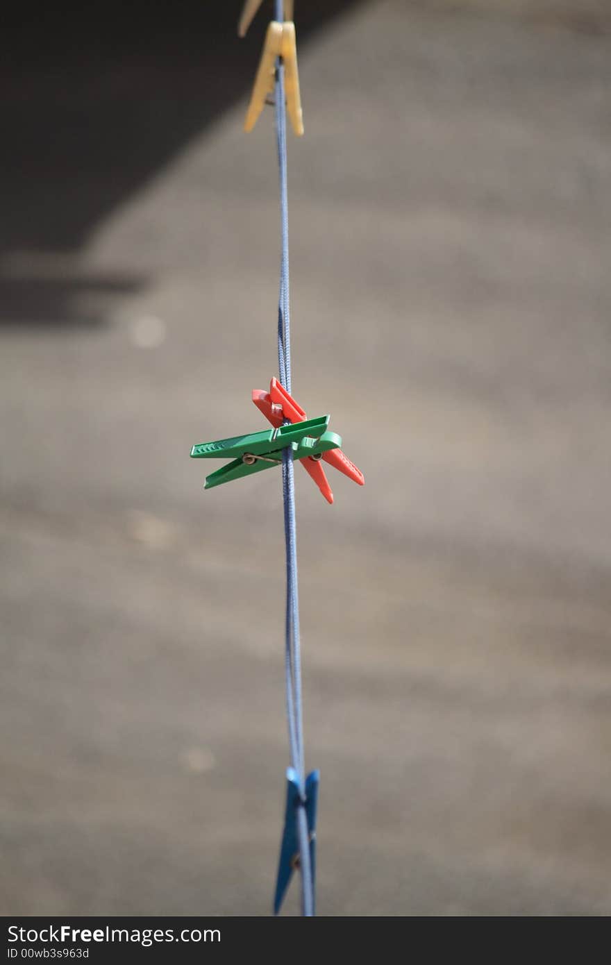 Multicoloured clothes-pegs hanging on blue rope on gray background